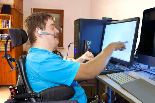 Young man in multifunctional wheelchair using a computer touchscreen, wearing headset